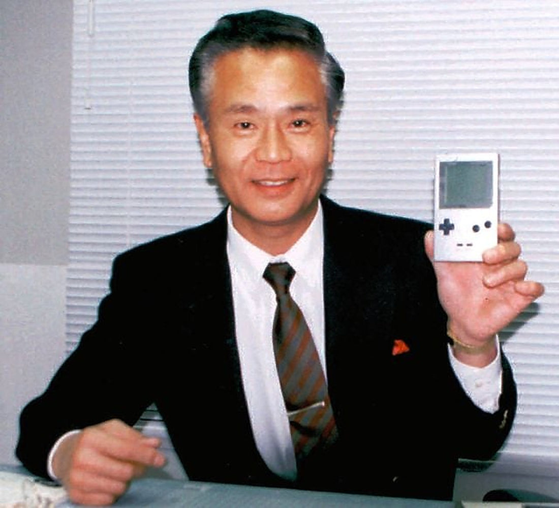 Gunpei Yokoi en costume, présentant une Game Boy face à l'objectif