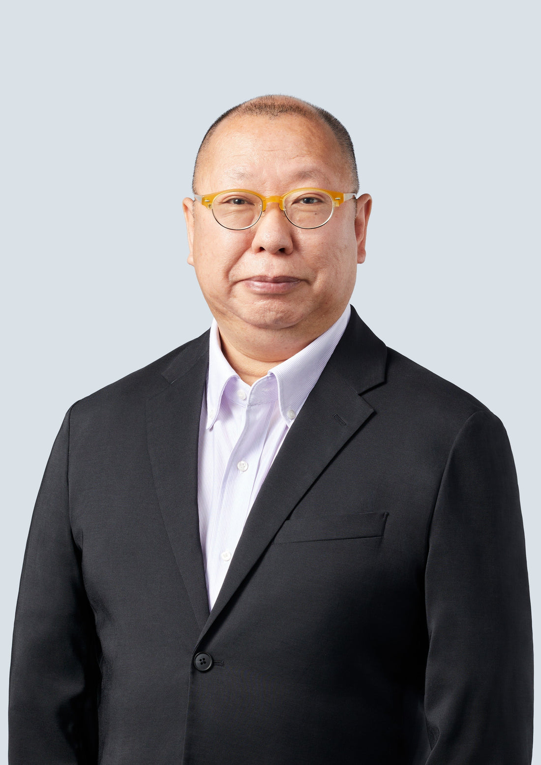 Portrait de Takashi Tezuka en costume sombre, sur fond gris clair