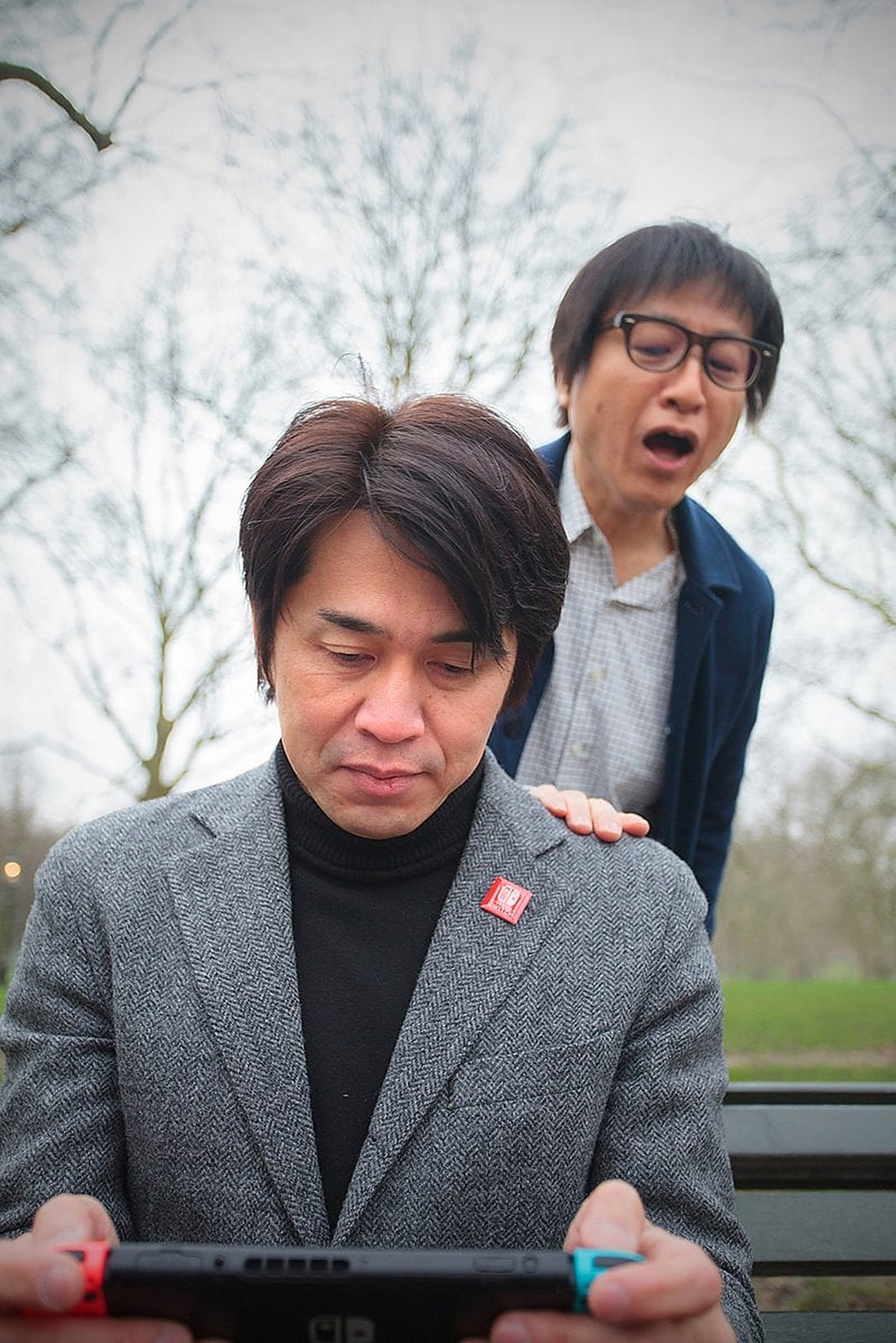 Yoshiaki Koizumi joue sur une Nintendo Switch en extérieur, un collègue penché derrière lui
